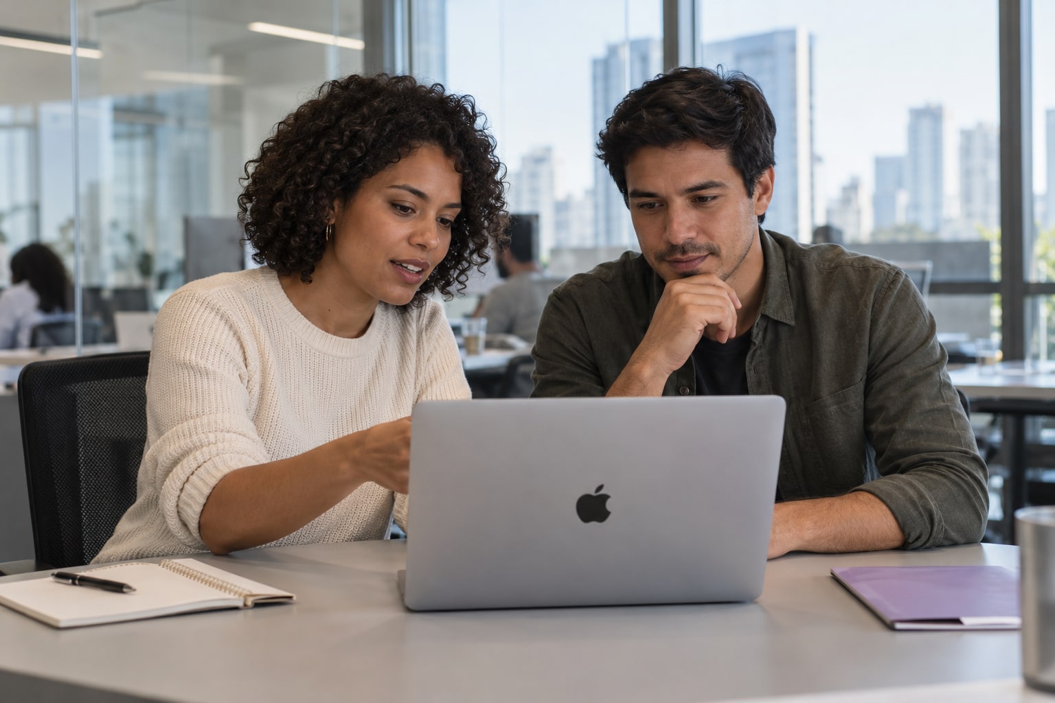 Two people reviewing a project on a MacBook in a modern office.
