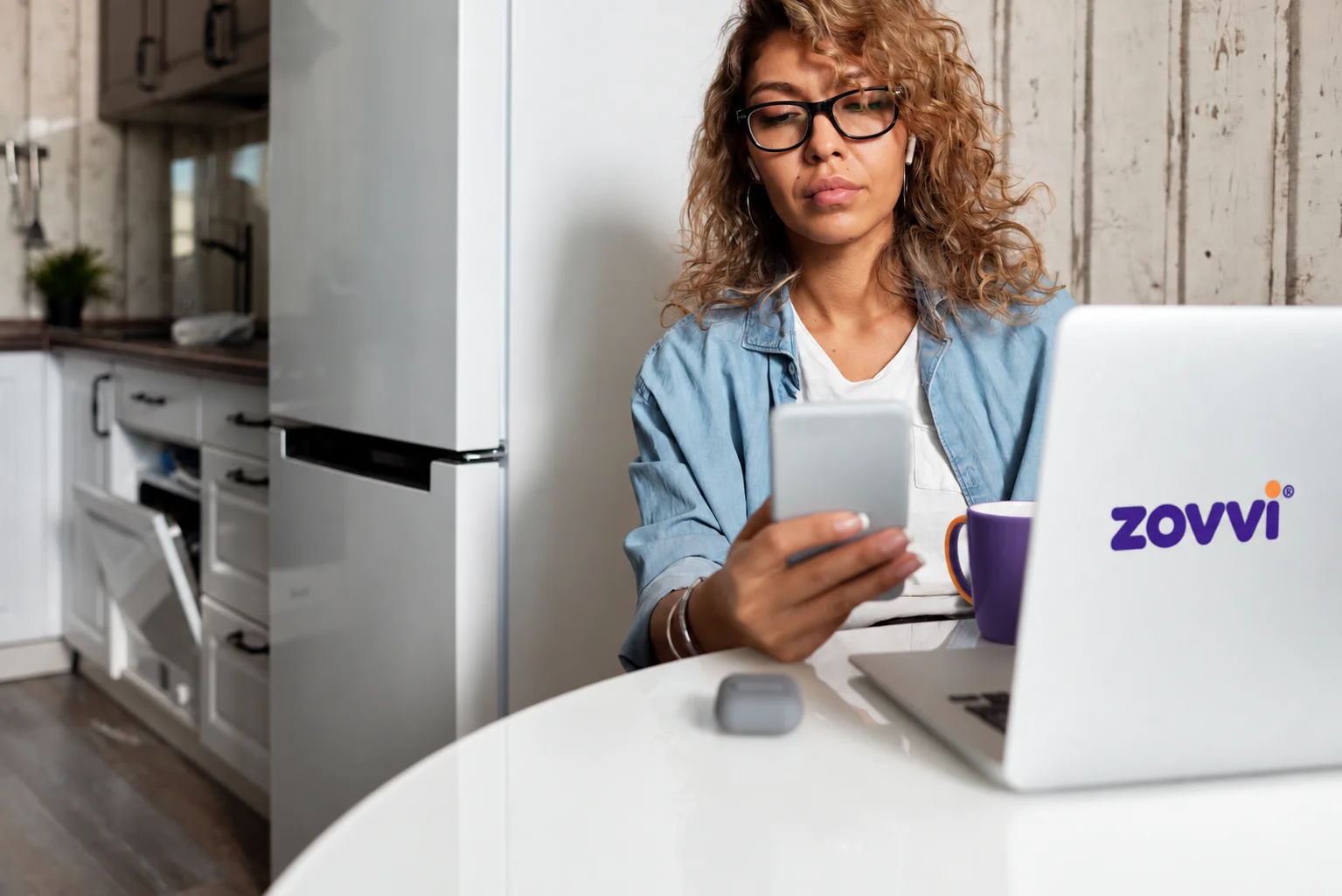 Person checking a phone while using a laptop at home